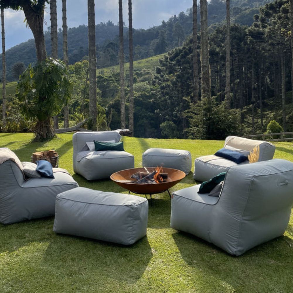 Espaço ao ar livre com poltronas puffs e uma lareira de fogo central, perfeito para encontros aconchegantes em meio à natureza, ilustrando uma decoração de natal para jardim.