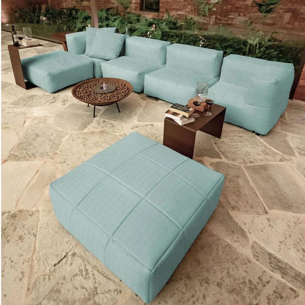 Sala ao ar livre em área aberta da casa com sofás modulares e pufes azuis, perfeita para relaxar em um ambiente moderno e acolhedor.
