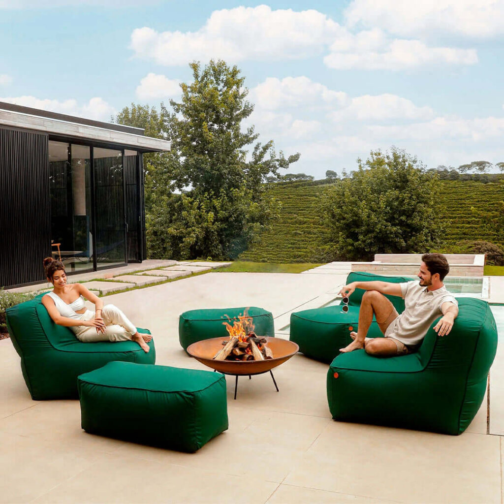 Conjunto de puffs verdes ao redor de uma lareira ao ar livre, uma opção moderna e aconchegante para decorar jardim.