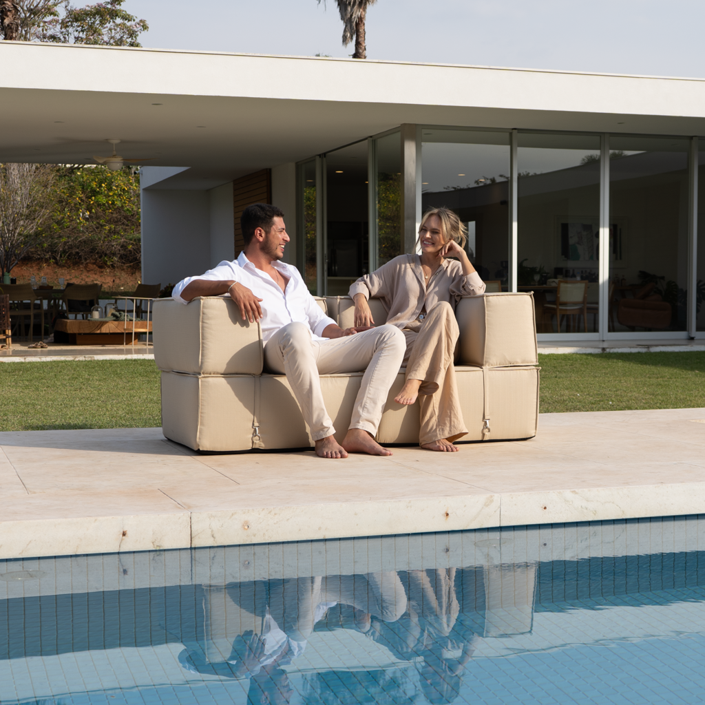 Casal aproveitando o sofá modular em área aberta da casa, próximo à piscina, com design moderno e integração com o ambiente externo.