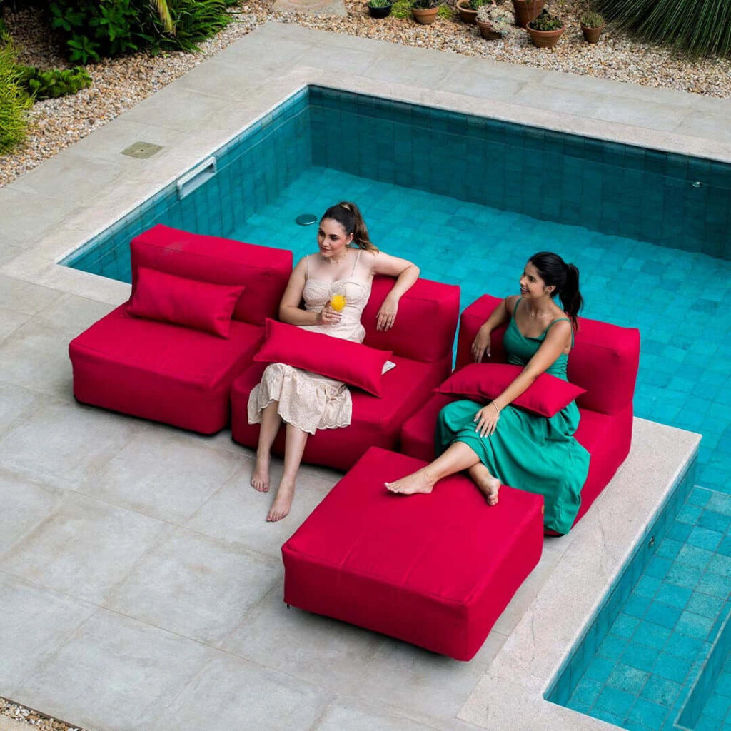 Decoração com sofás modulares vermelhos à beira da piscina, uma das ideias para área externa vibrante e descontraída.
