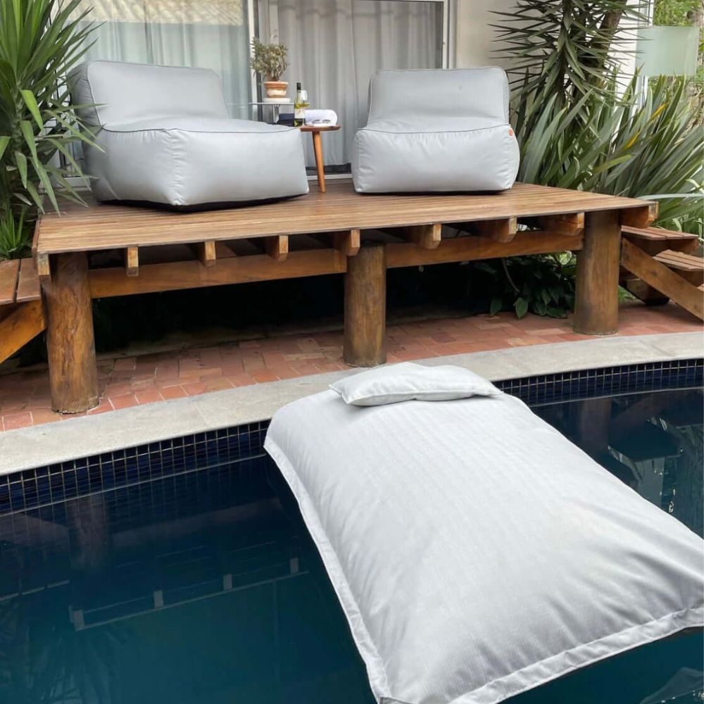 Puffs brancos e um puff flutuante em uma piscina, mostrando como decorar jardim com sofisticação e relaxamento.