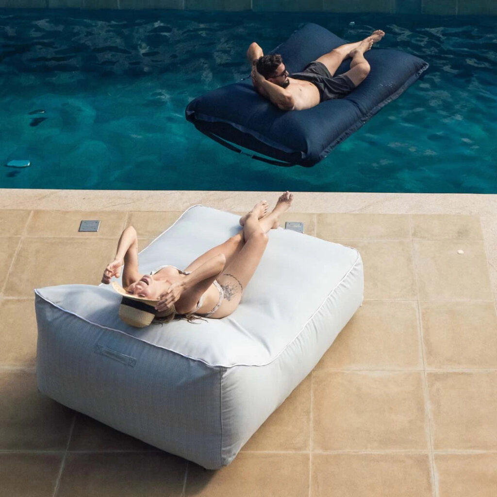 Espaço de lazer em área aberta da casa com puff poltrona confortável e tapete de piscina, ideal para relaxar ao sol e curtir momentos de descanso.
