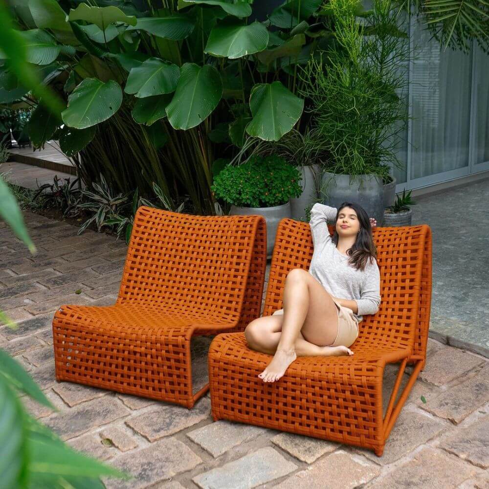 Poltronas tramadas laranja em um espaço ao ar livre com plantas ao fundo, destacando uma decoração elegante para jardim externo.